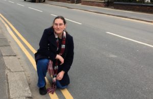 Cllr Zoë Kirk-Robinson kneeling on Park Road, with the double-yellow lines that are due to be removed.
